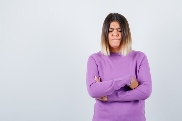 Cute woman holding arms folded in purple sweater and looking gloomy. front view.