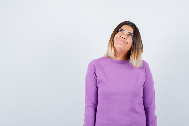 Cute woman looking up in purple sweater and looking dreamy , front view.