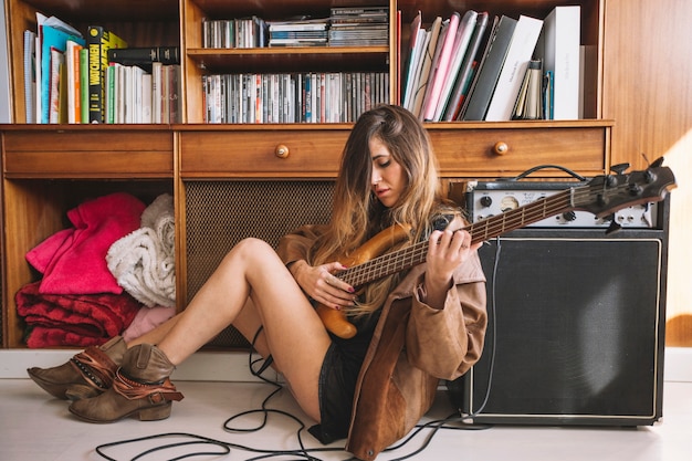 Foto gratuita donna carina che suona la chitarra sul pavimento