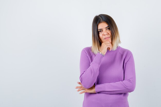 Cute woman in purple sweater with hand on chin and looking pensive , front view.