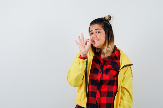 Cute woman in shirt, jacket showing ok gesture and looking cheery , front view.