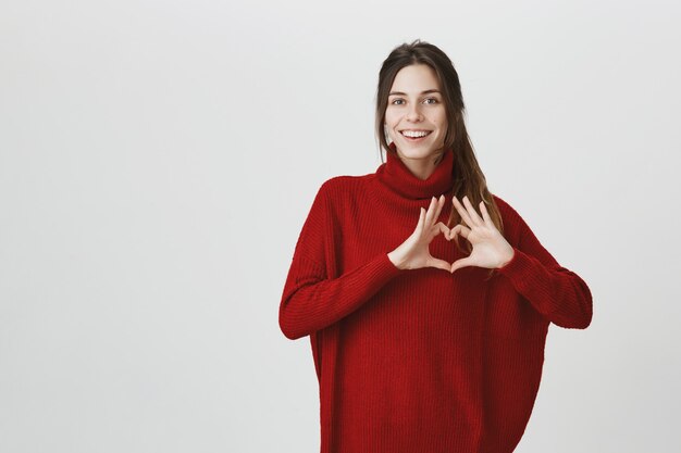 Cute woman in sweater show heart sign and smiling