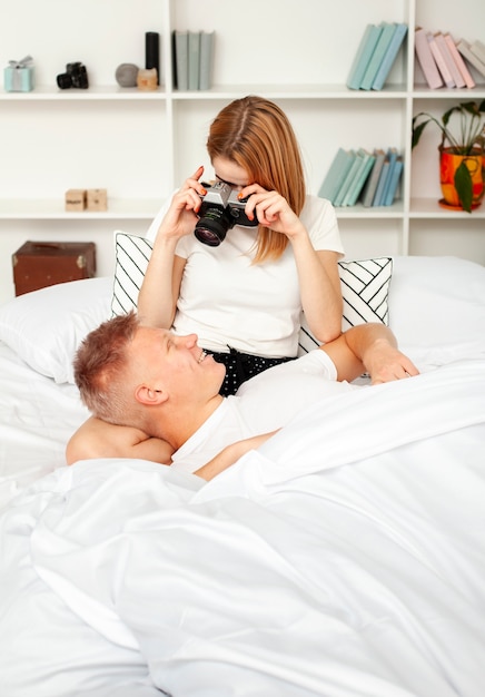 かわいい女性がベッドで彼女のボーイフレンドの写真を撮る