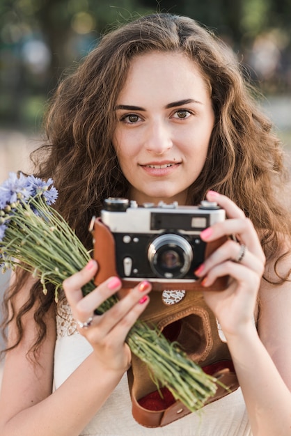 Foto gratuita donna carina con fotocamera e fiori