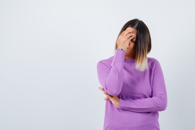 Cute woman with hand on face in purple sweater and looking upset. front view.