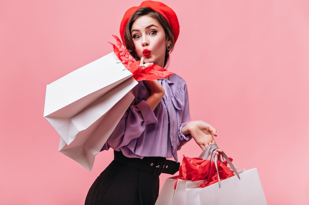 Free photo cute woman with red lipstick looks into camera and poses with white big bags after good shopping.