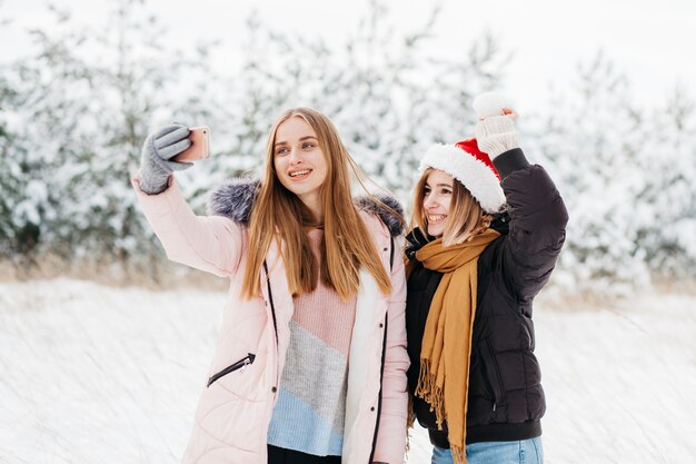 Cute women in Santa hat taking selfie in winter forest 