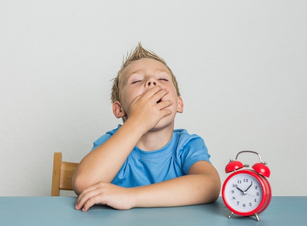 Free photo cute young boy with clock yawning