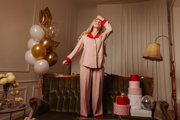 Free photo cute young caucasian blonde woman spends her free time at pajama party among gifts and balloons holiday concept