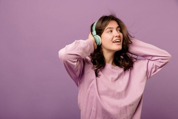 Cute young caucasian brunette girl listens to music in headphones looking away on purple background Audio concept