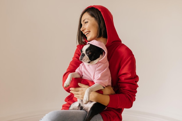 La giovane donna caucasica carina indossa una felpa con cappuccio rossa tiene in mano il cane in felpa rosa concetto di stile di vita e amicizia