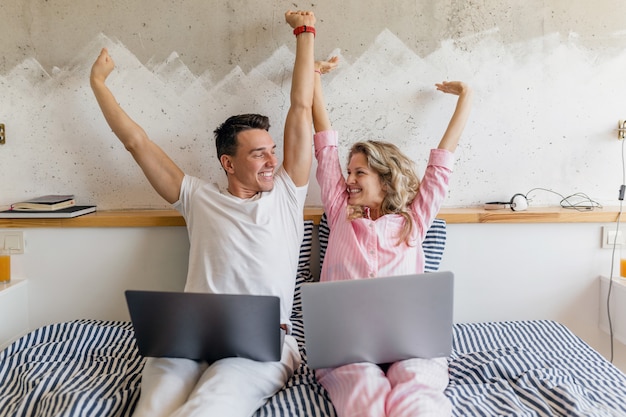 Cute young couple on bed in morning, man and woman holding laptop, working onlinestretching