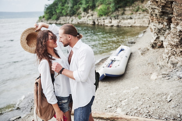 かわいい若いと川の背景のカップル。バックパックを持った男と女がボートで旅行しています。旅行者の夏のコンセプト