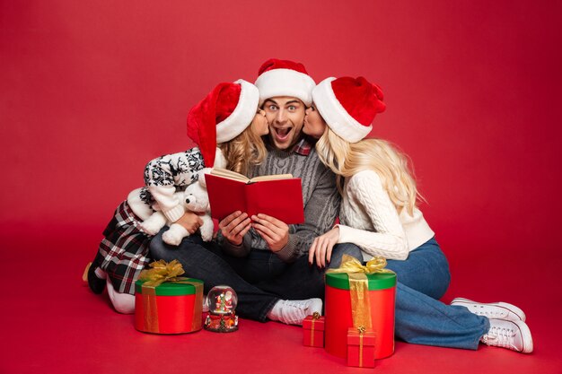 Cute young family wearing christmas hats sitting isolated