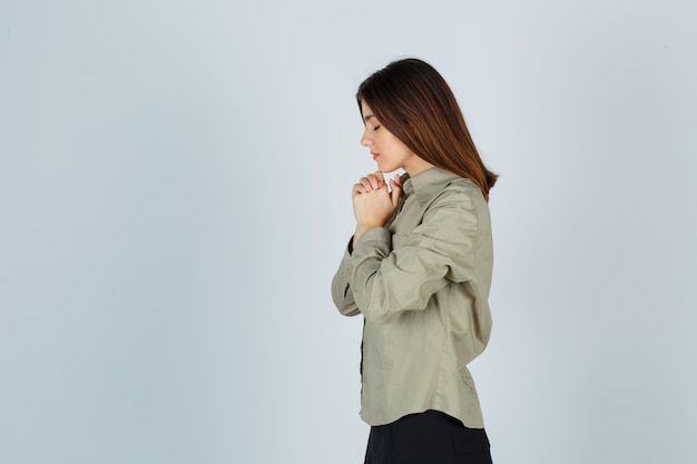Free photo cute young female clasping hands in praying gesture in shirt, skirt and looking hopeful .