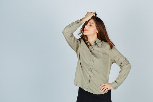 Cute young female combing hair back in shirt, skirt and looking relaxed , front view.