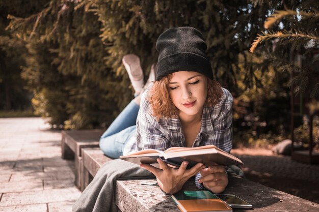 Cute young female in hat reading book in park