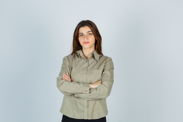 Cute young female holding arms folded in shirt, skirt and looking sensible. front view.