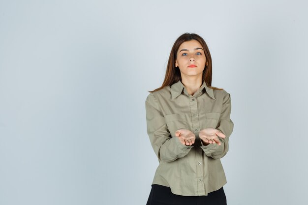 Cute young female making giving or receiving gesture in shirt, skirt and looking sensible. front view.