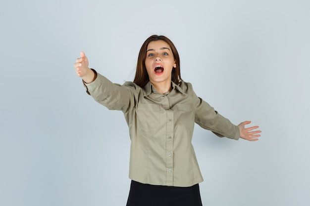 Cute young female opening arms for hug in shirt, skirt and looking wondered. front view.