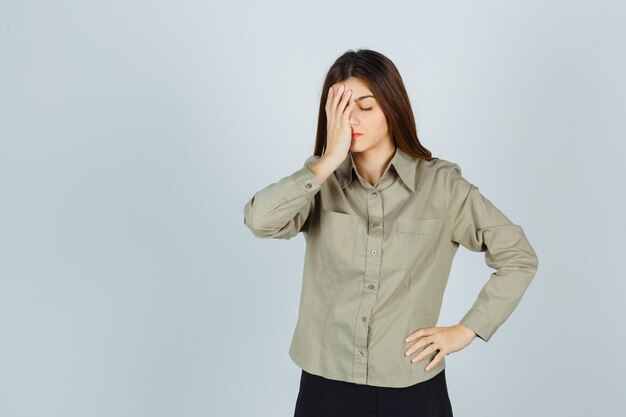 Cute young female in shirt, skirt holding hand on face and looking distressed , front view.