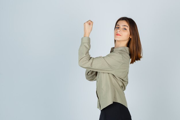 Cute young female showing muscles of arm in shirt, skirt and looking confident .