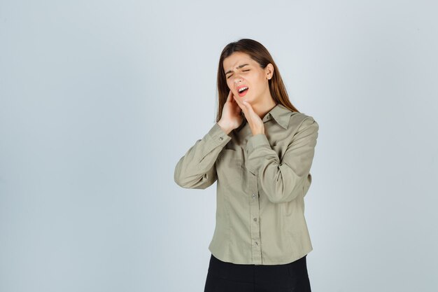 Cute young female suffering from toothache in shirt, skirt and looking painful , front view.