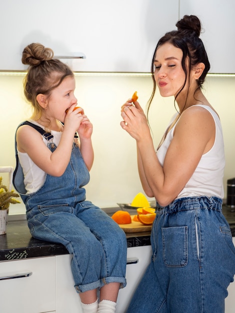 Free photo cute young girl eating orange with mother