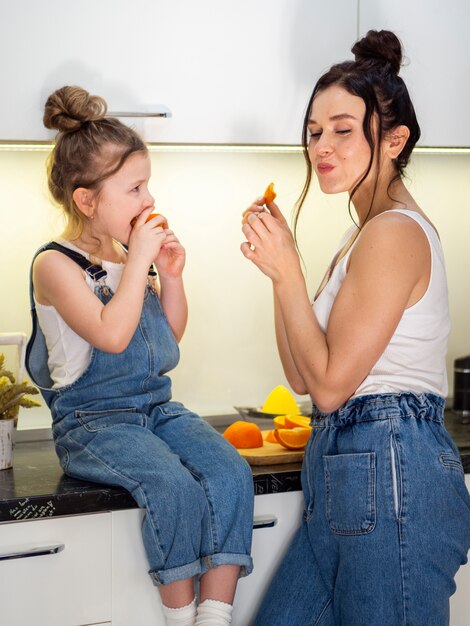 Cute young girl eating orange with mother