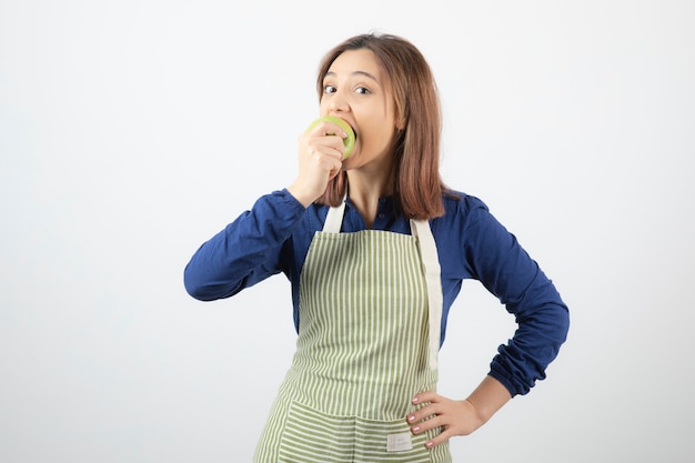 Un modello di ragazza carina in grembiule che mangia una mela fresca verde.