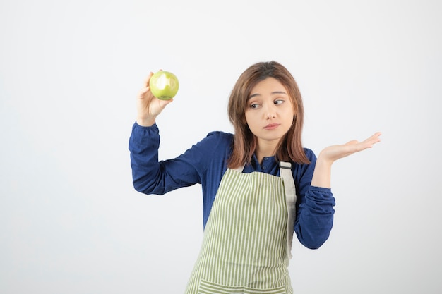 a cute young girl model in apron holding a green fresh apple.