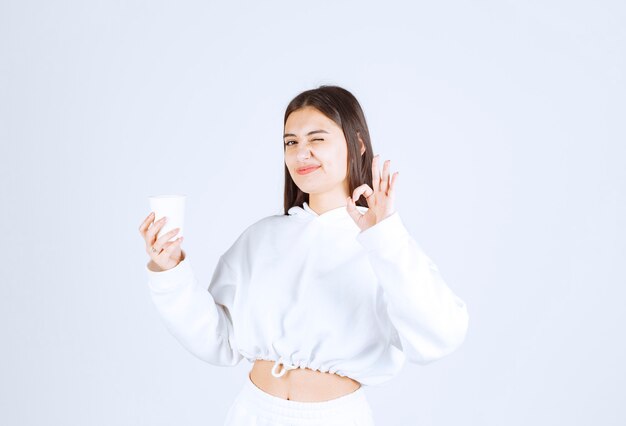 cute young girl model with a plastic cup showing ok gesture.