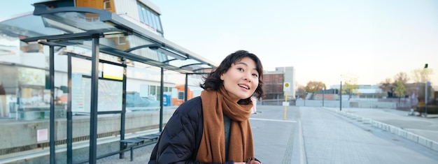 Free photo cute young girl student waiting on a bus stop looking for her public transport on app tracker