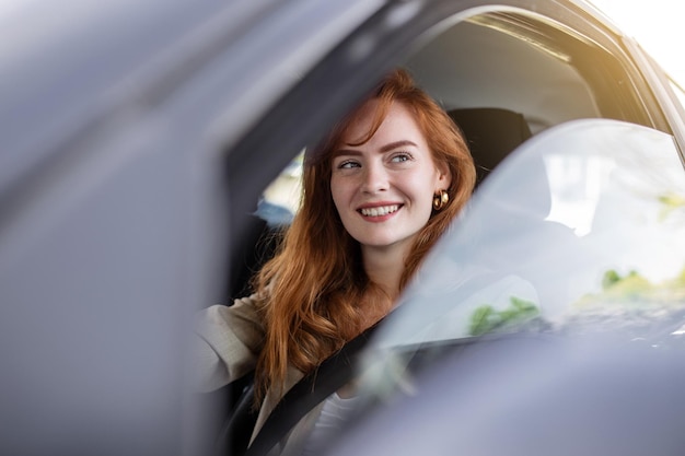 Cute young lady happy driving car Image of beautiful young woman driving a car and smiling Portrait of happy female driver steering car with safety belt
