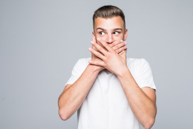Cute young man boy close his mouth with arms isolated on white wall