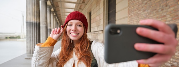 無料写真 かわいい若い赤毛の女性が路上で携帯電話で自分撮りをし、自分の写真を撮る