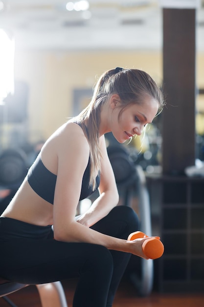 cute young woman in gym with dumbbells