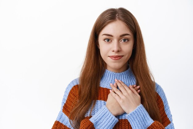 Cute young woman holding hands on heart keep romantic warm memories in soul being grateful for praises say thank you standing over white background