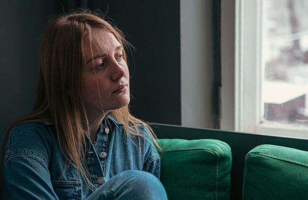 A cute young woman is sitting on the sofa by the window