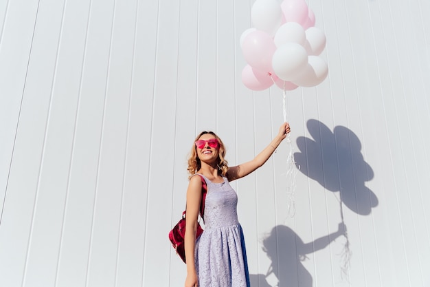 Cute young woman in pink sunglasses enjoying the sunny day, holding air balloons