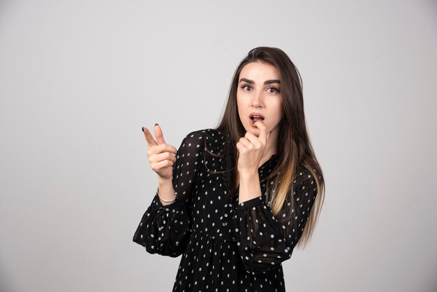 Cute young woman pointing a finger away on a gray wall.