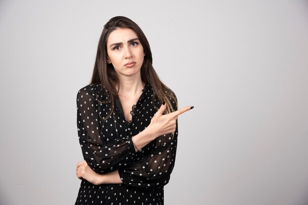 Free photo cute young woman pointing a finger away on a gray wall.