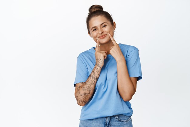 Cute young woman smiling, showing her dimples on cheeks, standing lovely in blue tshirt against white background