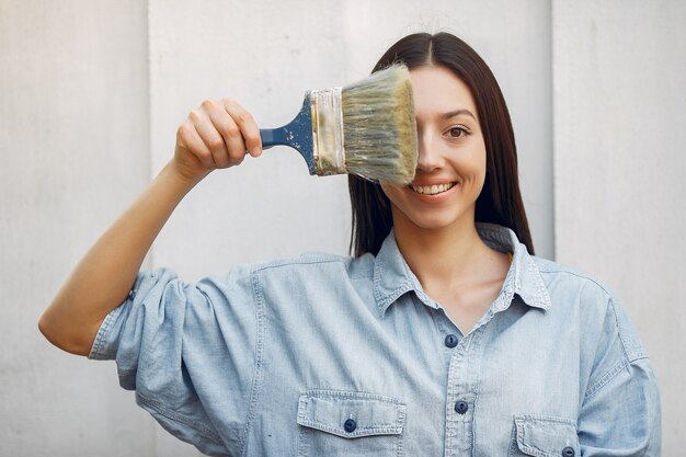 Cute young woman standing near wall with brush