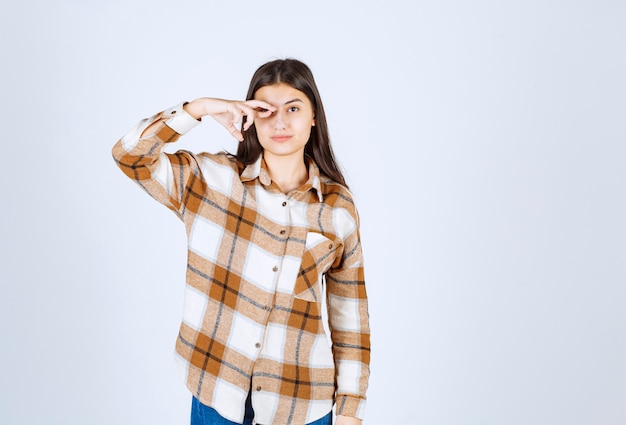 Cute young woman standing on white wall.