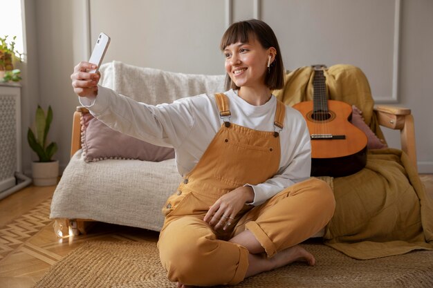 Cute young woman taking a selfie next to her guitar