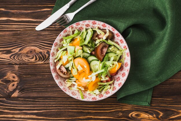 Cutlery and napkin near bowl with salad