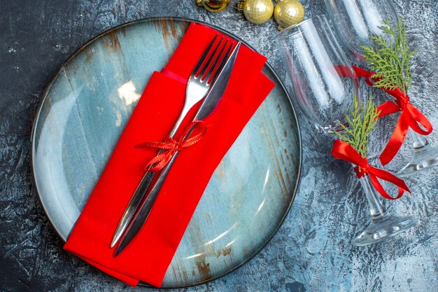 Cutlery set on a blue plate and fallen glass goblets next to decoration accessories on dark background horizontal view