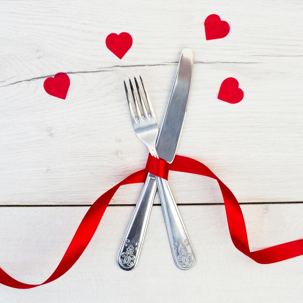 Cutlery with red ribbon near ornament hearts