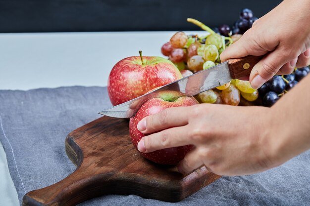 Cutting an apple on the fruit board with grapes around. 